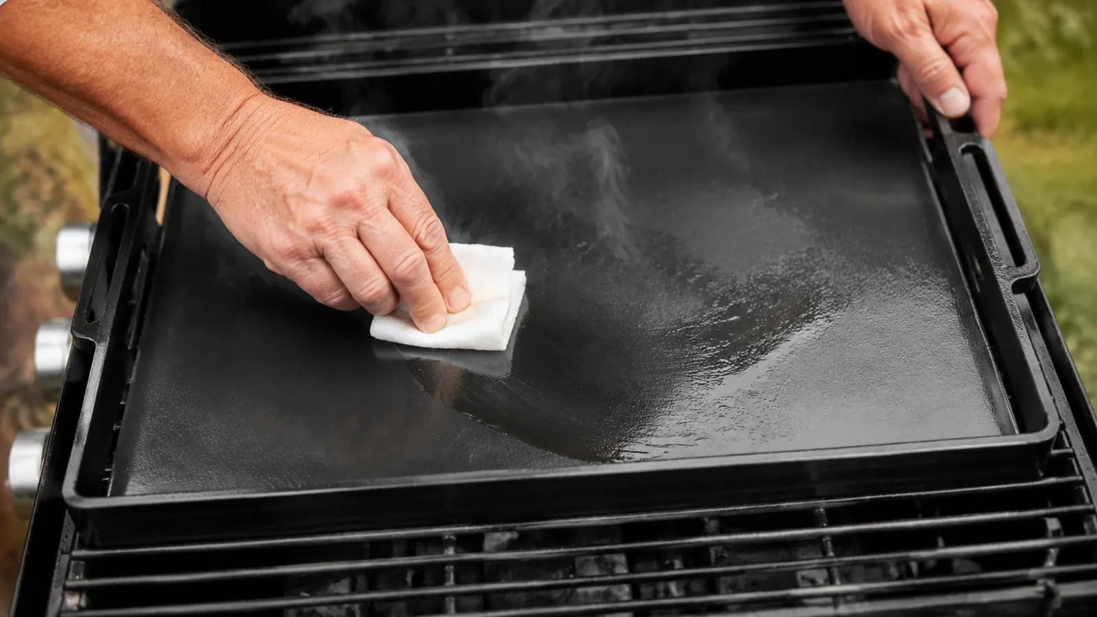 Hand spreading oil over a cast iron griddle with a folded cloth during seasoning